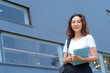 © Ardianto - A woman is smiling and holding a cell phone and a book. She is wearing glasses and a backpack