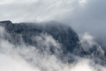 Wall Mural - Prominent rocky mountains surrounded by mist and clouds and creating a rugged and magical setting