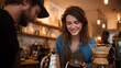© venusvi - A young woman smiles at a barista while enjoying a freshly brewed coffee in a cozy cafe setting.