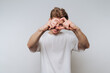 © bodnarphoto - Young man in a white t-shirt making a heart shape with his hands against a plain background.