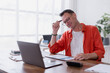 © Tj - Businessman holding a pen to his head, analyzing financial charts on his laptop in a modern office, feeling the weight of stress and fatigue while tackling complex data