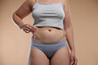 © New Africa - Liposuction. Woman in underwear touching her belly on beige background, closeup