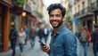 © Vadym - Latin American man smiles holding smartphone on busy street. He wears a denim shirt. Background shows blurred people and shops. Modern communication and connection theme.