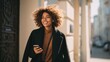 © Johannes - cheerful african woman holds smartphone curly brunette lady in brown blouse and black coat smiles and walks outdoors no logos no brands ar 169