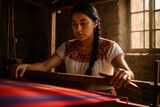 Young Mexican woman with braided hair in an embroidered white blouse weaving vivid red and blue striped fabric on a loom.