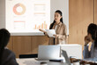 © fizkes - Data driven seminar. Young Asian woman speaker lead interactive presentation in modern meeting room use digital screen to visualize project information in charts graphs give report to diverse audience