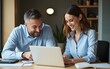 © fu - Vertical portrait of mature Latin business man and European business woman discussing project on laptop in office. Two diverse confident professional partners colleagues business people work together.
