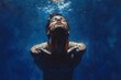 © oio - Man submerged underwater with head tilted back toward the surface, light filtering through water creating dramatic shadows and reflections