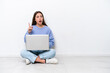 © luismolinero - Young caucasian woman with laptop sitting on the floor isolated on white background thinking an idea pointing the finger up
