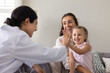 © fizkes - Happy Indian woman pediatrician in uniform gives high five to cute little 3s girl, kid smiling while sits on her mother lap during doctor home visit. Trust, pediatric care, stress-free medical support