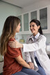 © fizkes - Happy satisfied young Hispanic female doctor touching shoulder and hand of cheerful patient woman, discussing successful rehabilitation, recovery after beating disease. Vertical shot