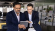 © fizkes - Two focused diverse young and mature businessmen browsing professional social media on tablet. Younger employee giving help to elder colleague with online application work. Banner shot