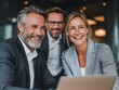 © CHAIYAPHON - Three successful business colleagues smile confidently while collaborating on a laptop in modern office space.
