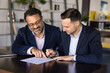 © fizkes - Senior Indian businessman pointing finger at place for signature in document for younger business partner signing. Real estate, insurance agent, notary meeting with client