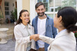 © fizkes - Woman realtor greeting couple with handshake gesture. Clients and real estate agent shaking hands, accept contract details, make property deal standing outdoor. Loan, buying first, affordable house