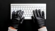 © Nataliia_Trushchenko - Person wearing black gloves is typing on a keyboard. The gloves are black and the person's hands are visible. Concept of mystery and secrecy