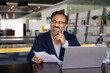 © fizkes - Cheerful senior Indian business leader man doing paperwork job in co-working office workplace, analyzing paper reports, legal financial documents, looking away, thinking, smiling, laughing