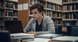 © Muhammad - Focused young man studying in library using laptop books education research student college university learning knowledge technology academic success