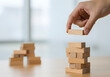 © Creative Creating - Building a business structure with wooden blocks. A hand carefully adds another level to a block tower, symbolizing strategic growth, project development, and building a strong foundation with precisi