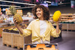 © anatoliycherkas - Woman choosing between pineapple and melon in supermarket