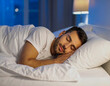 © theshooter - Un hombre joven dormido descansando durante la noche en la cama con sabanas y almohada blanca con la luz del dormitorio encendida concepto de sueño y la importancia del descanso y una vida saludable