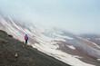 © Soloviova Liudmyla - Lonely female backpacker dressed rain cover with backpack and trekking poles making acclimatization trek around Lenin peak base camp climbing Petrovsky Peak 4910 m, Pamir mountains range, Kyrgyzstan.