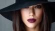 © Unique Image - Elegant woman with brown eyes and plum lips face partially hidden by a wide-brimmed black hat.