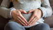 © BEAUTY - Pregnant woman forming a heart shape with her hands on her belly