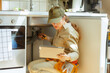 © Alliance - A female plumber kneels under a kitchen sink with a wrench and tablet, inspecting a pipe blockage and combining hands-on work with digital tools.
