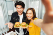 © InfiniteFlow - Smiling host chef influencers taking photo with smartphone by selfie straight view holding double hamburger on cooking show special easy dish homemade on social media channel live streaming. Infobahn.