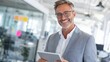 © Formoney - A confident business professional stands in a contemporary office space, smiling while holding a tablet. Natural light fills the area, enhancing the inviting atmosphere.