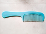 Blue plastic hair comb with handle on white textured background, perfect for hair care products, beauty accessories, personal grooming tools, salon equipment, and everyday hygiene concept photography.