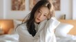 © 沈军 贡 - A young woman with long hair, wearing a white sweater, leans on a pillow in a cozy bedroom with soft lighting, exuding a relaxed and calm atmosphere.