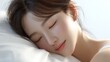 © 沈军 贡 - A young Asian woman rests peacefully on a soft white pillow, showing a state of calm and relaxation during sleep.