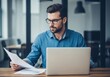 © SHAPLA - Focused businessman in blue shirt analyzing documents with laptop
