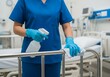 © Agung - Healthcare professional in blue scrubs sanitizing a hospital bed rail with disinfectant spray and cloth