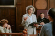 © AnnaStills - Caucasian middle aged woman lawyer addressing courtroom while holding folder, Caucasian teenage boy sitting at witness stand, judge and another woman present in background