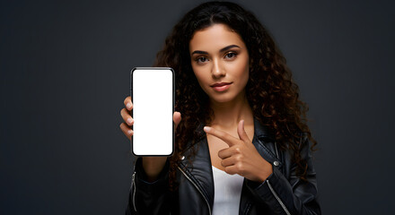 Woman in leather jacket pointing at smartphone with blank white screen, dark background, perfect for marketing or app promotion.