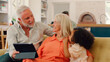 © Monkey Business - Granddaughter And Grandparents On Sofa At Home Streaming Show On Digital Tablet