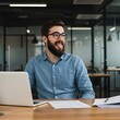 © Taposh - Bearded man in blue shirt working on laptop in modern office