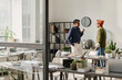 © TrueFrame Collective - Wide shot of two Indian male coworkers standing in modern office, talking during coffee break, copy space