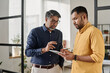 © TrueFrame Collective - Medium shot of two Indian men standing in office looking at digital tablet screen discussing business plan