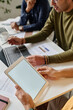 © TrueFrame Collective - Vertical high angle shot of unrecognizable man sitting at table at business meeting holding digital tablet with blank screen