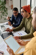 © TrueFrame Collective - Vertical over-the-shoulder shot of three Indian men sitting at table in modern office working on business project together