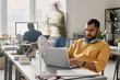 © TrueFrame Collective - Young South Asian man wearing yellow shirt sitting at desk in modern office working on laptop, copy space