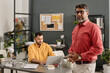 © TrueFrame Collective - Selective focus medium shot of modern mature Indian manager wearing smart casual clothes standing in office looking at camera