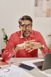 © TrueFrame Collective - Vertical medium portrait of confident mature Indian man sitting at office desk looking at camera