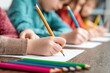 © oksa_studio - Close up view of children drawing with colored pencils on blank sheets of paper in an elementary school classroom