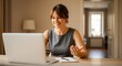 © HRIDOY - A young woman smiling while working on her laptop at home, participating in a video conference call or online webinar.