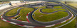 © AmazingAerialAgency - Concord, United States - 28 July 2025: Aerial view of a race track's winding asphalt curves cutting through vibrant green fields, contrasted by the stark white and red safety barriers.